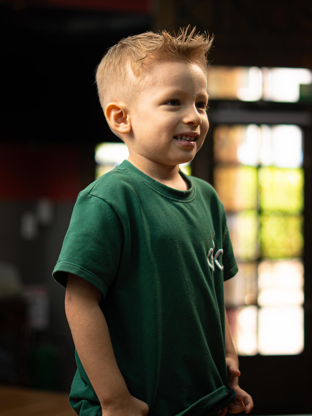 Niño sonriente con camiseta verde de Kings Cave