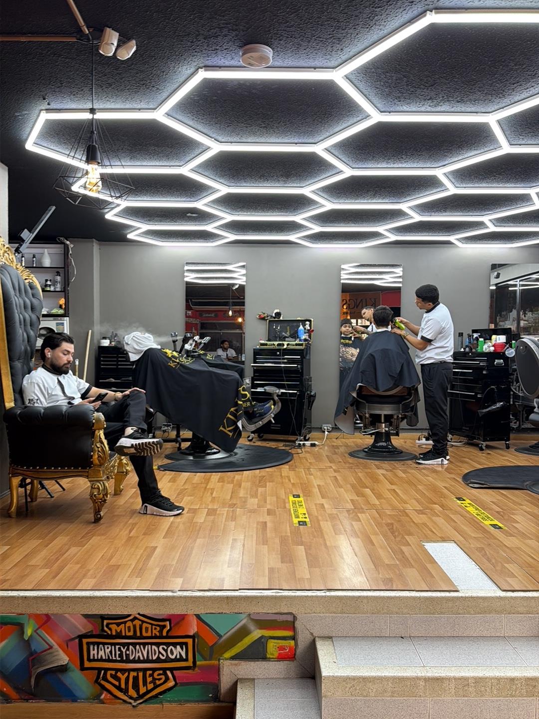 El salón de Kings Cave: trono negro con dorado, sillas de barbería y techo de luces hexagonales